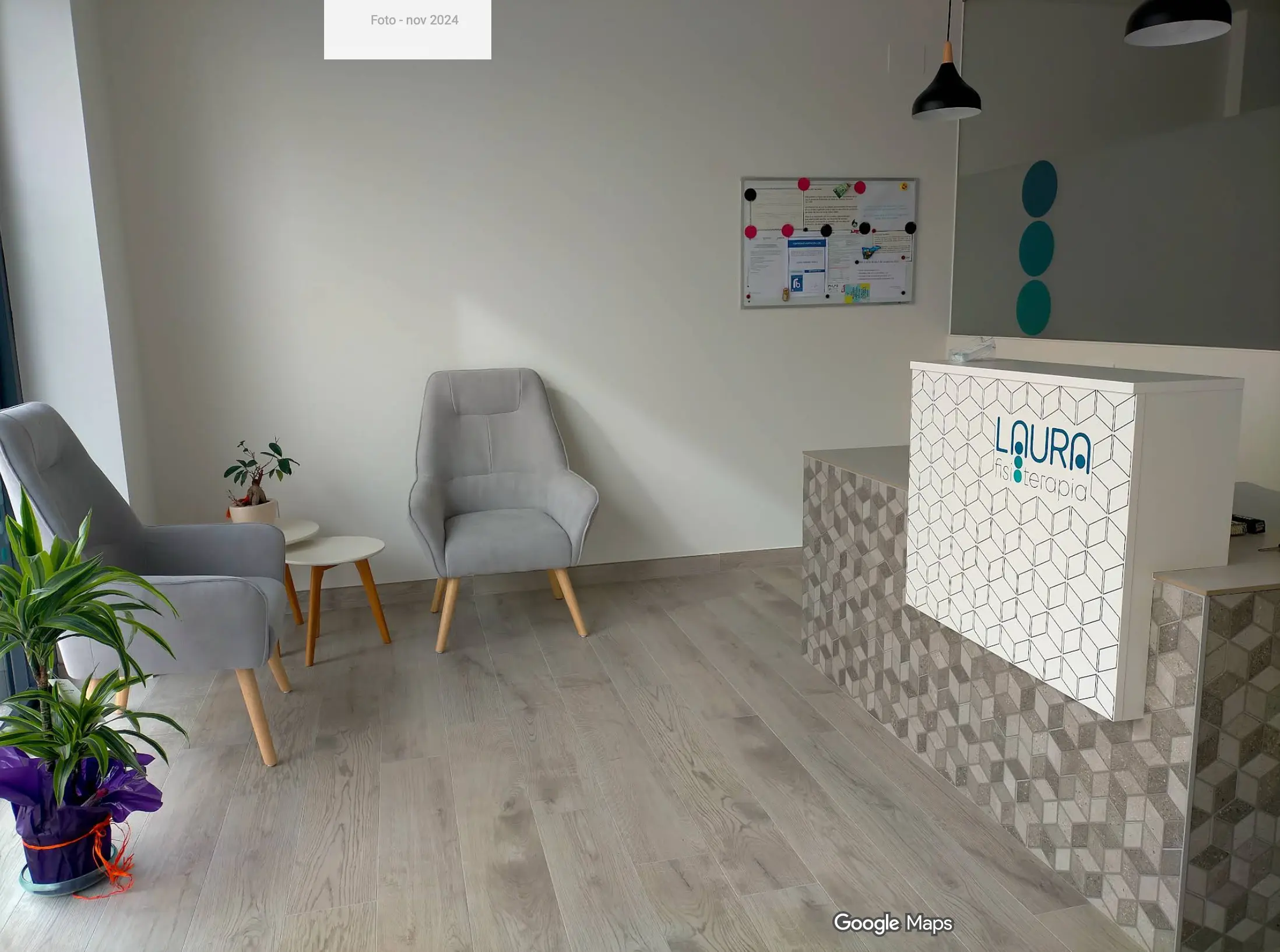 Sala de espera con sillones grises, una mesa auxiliar de madera y el mostrador de recepción con el logotipo de la clínica
